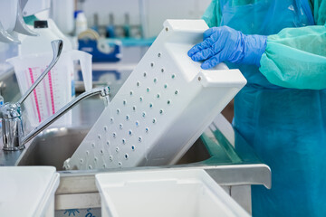 Close-up of healthcare worker's gloved hands cleaning medical instrument tray under running water...