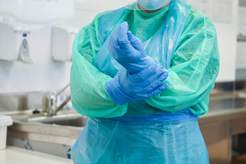 Close-up of a healthcare worker wearing green gown and blue apron, meticulously adjusting medical gloves for stringent safety protocols and clinical environment protection