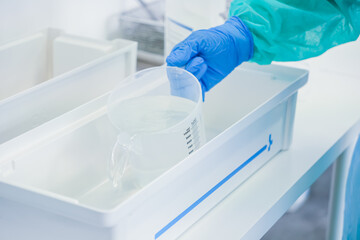 Close-up view of a medical worker's gloved hand accurately pouring solution from a clear graduated...