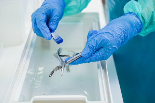 Close-up of gloved hands meticulously scrubbing surgical instruments with a small brush in a container, part of the crucial sterilization process in healthcare