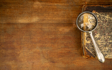 An antique hardcover book lies on a wooden table, next to a magnifying glass.Vintage library.