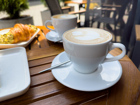 A white coffee cup of cappuccino on a wooden table with a plate of croissants. breakfast in cafe, Paris morning, Europe morning. High quality photo