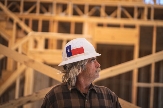 Construction Worker Wearing Hard Hat with Texas Flag Sticker Walking Inside Wooden Frame of House at Construction Site
