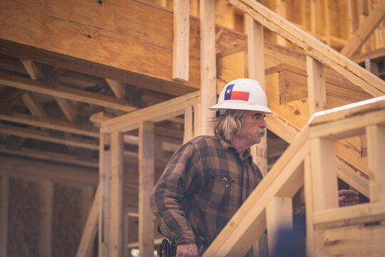 Construction Worker Wearing Hard Hat with Texas Flag Sticker Walking Up Stairs Inside Wooden Frame of House at Construction Site