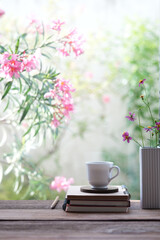 White coffee cup with notebook and pink flowers by the window