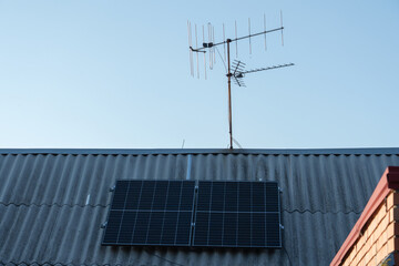 Rooftop solar panels and antennas against a clear blue sky at sunset in a residential area