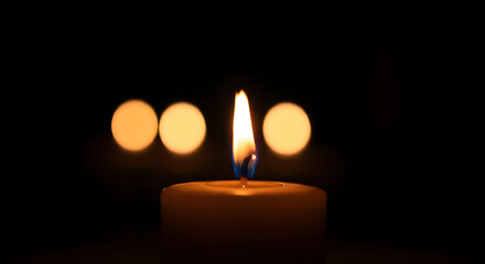 Candle flame illuminating dark background with blurred bokeh lights  