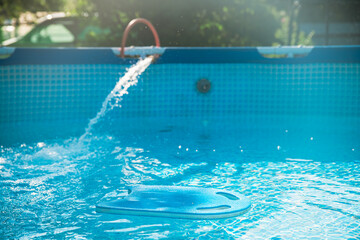 Crystal clear fresh water is being poured into a home garden pool from a garden hose on a sunny summer day, providing a refreshing escape from the heat