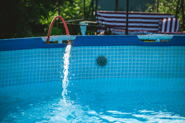 Crystal clear fresh water is being poured into a home garden pool from a garden hose on a sunny summer day, providing a refreshing escape from the heat