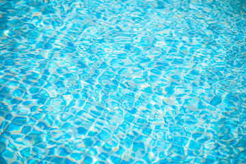 Crystal-clear turquoise blue pool water surface is gently rippling, reflecting sunlight and revealing the mosaic tiles beneath, creating a refreshing and inviting summer scene