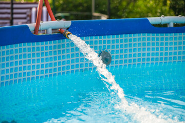 Crystal clear fresh water is being poured into a home garden pool from a garden hose on a sunny summer day, providing a refreshing escape from the heat