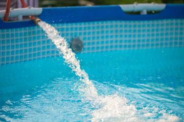 Crystal clear fresh water is being poured into a home garden pool from a garden hose on a sunny summer day, providing a refreshing escape from the heat