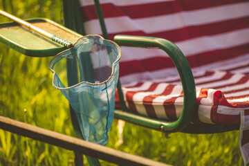 Blue butterfly net hanging from a green and red striped garden swing captures the essence of summer leisure, inviting memories of childhood adventures and playful moments in nature
