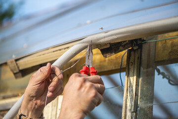 Electrician is working on the electrical wiring of a greenhouse, carefully stripping and connecting cables using pliers and a wire stripper, ensuring proper insulation and safety measures