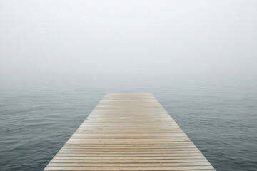 Obraz premium Endless wooden pier stretches over calm water in foggy atmosphere