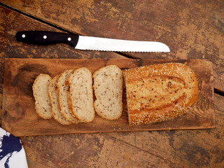 A loaf of bread with seeds on it is placed on a wooden cutting board, and a knife with a black...