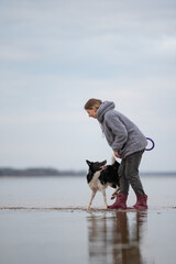 A woman in a gray hoodie and red boots interacts with her energetic black and white Border Collie...