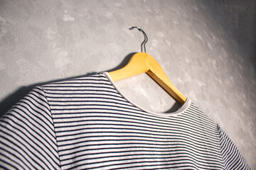 Stripped t-shirt on wooden hanger against grey wall in home interior.