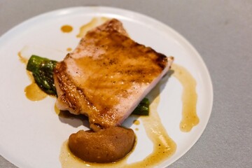 close up of grilled pork loin ( pork chop) with Caramelised Apple sauce resting on a bed of vibrant green asparagus on a white and grey plate