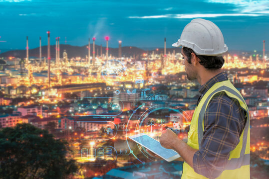 Engineer with tablet monitoring smart oil refinery at night with digital interface overlay.