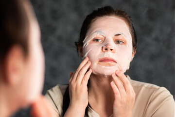 Side view of female carefully placing facial sheet mask. Useful for demonstrating proper skincare...