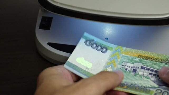 Examination of Lao Kip (LAK) cash money with UV counterfeit detector. Concept of authenticity check, fight against counterfeiting of banknotes, anti fraud measures in Laos. Close up view.