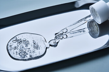 A pipette with cosmetic serum on a blue background.