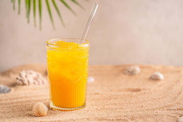 Colourful orange cocktail in a tall glass on a sand of a golden beach at a tropical holiday resort...