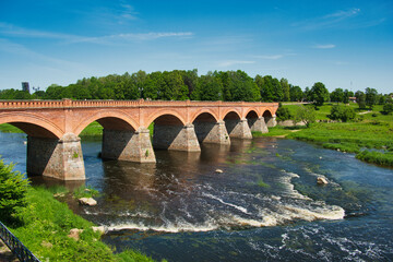 Fototapeta premium Kuldīga's Iconic Red Brick Bridge and Venta River in Summer