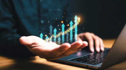 A hand floats palm-up above a laptop showing glowing cyan arrows and yellow candlestick charts against a dark teal background with soft lighting