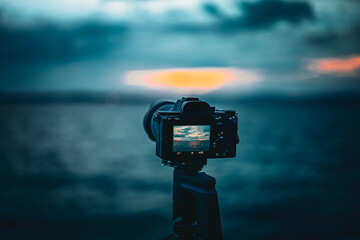 A close-up shot of a digital camera on a tripod, capturing a serene lake sunset with dramatic blue and orange tones in Switzerland.