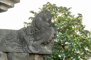 A detailed stone carving of a mythical creature at Borobudur, with trees in the background.