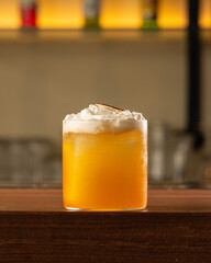 Glass of yellow colour cocktail with white foam as garnish over a bar counter