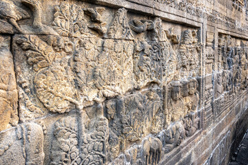 Stone wall carvings show ancient scenes with trees, people, birds, and animals in fine detail.