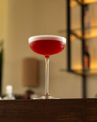 Glass of pink colour cocktail with white foam as garnish over a bar counter