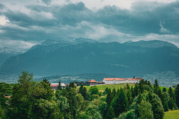 Panoramic view of a historic Swiss monastery surrounded by green forest with dramatic alpine...