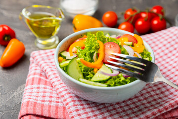 Cucumber salad on a wooden background.Homemade salad with fresh vegetables, cucumber, tomato, sweet pepper and lettuce in a plate.Vegetarian spring salad.Vegetarian diet.Healthy eating.Space for text