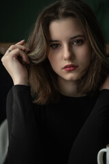 Fototapeta premium Portrait of a young beautiful long-haired girl in dark clothes in an interior studio.