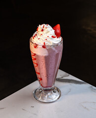 Strawberry Milkshake with Whipped Cream and Syrup in Tall Glass on Marble Table