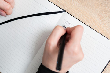 Writing a to-do list in a notebook with a black pen on a wooden table during the day