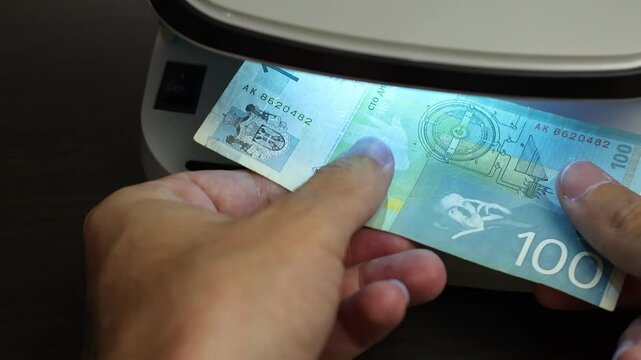 Examination of Serbian Dinar (RSD) cash money with UV counterfeit detector. Concept of authenticity check, fight against counterfeiting of banknotes, anti fraud measures in Serbia. Close up view.