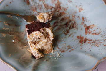 An uneaten piece of cake on blue vintage plate. Slice of tiramisu with fork on plate, close up. Delicious chocolate biscuit for breakfast. Sweet food concept. Italian dessert. Dirty plate with cake.