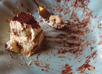 An uneaten piece of cake on blue vintage plate. Slice of tiramisu with fork on plate, close up. Delicious chocolate biscuit for breakfast. Sweet food concept. Italian dessert. Dirty plate with cake.