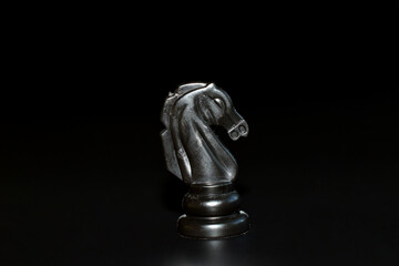 A chess piece, a knight, black on a black background.