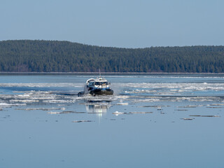 A hovercraft moves on the calm water of a lake, ice floes float on the surface of the water on a...