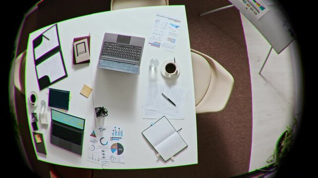 Fish eye directly above shot of white work table with laptops, folder with documents, notebooks, sticky notes, cups of coffee in empty office