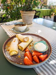 A delicious sweet breakfast with cheese-filled crepes (blini), fresh strawberries, and sour cream, served with tea in a cozy cafe.A healthy and tasty brunch in a restaurant.