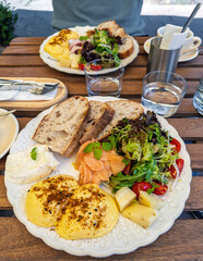 Close-up of a balanced breakfast meal on a decorative plate.A savory breakfast served at an outdoor cafe, featuring a generous platter with benedict eggs, salmon, fresh salad, and bread.