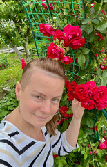 50 year old woman poses in her garden with roses in the background.