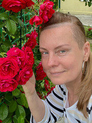 50 year old woman poses in her garden with roses in the background.